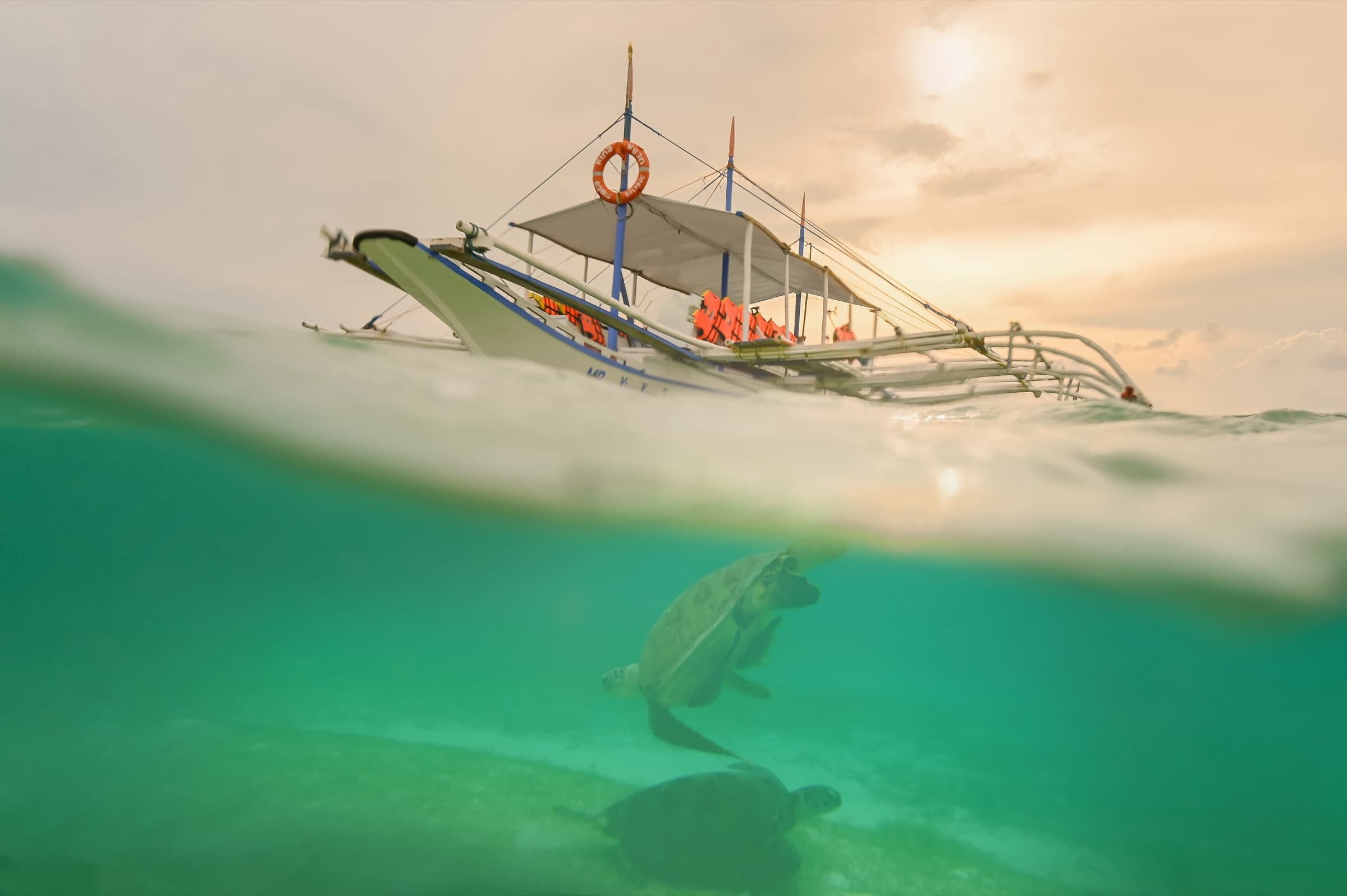 A sea turtle below the waterline and a bangka above it at Onok Island, Balabac